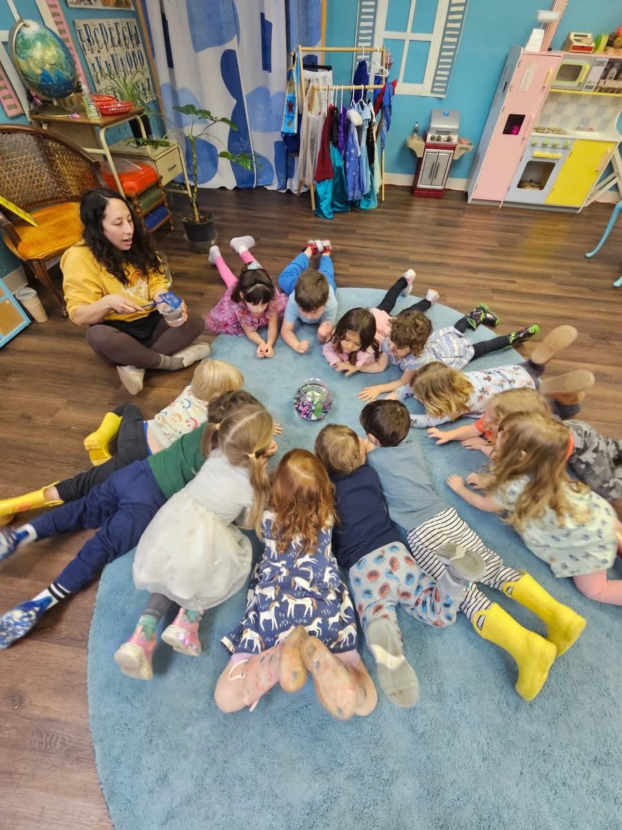 Children lying in a circle on the rug, watching a fishbowl